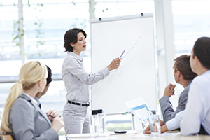 Business meeting with woman pointing at chart on freestanding white board.