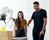 Two people viewing a robotic arm