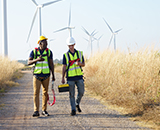 Two men walking down a dirt road with wind turbines in the background