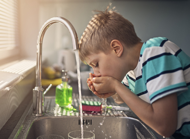 child drinking water from a tap, highlighting it's safe and passes regulations